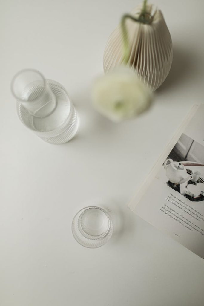 Minimalist arrangement featuring a glass vase, water glass, and magazine on a white surface.